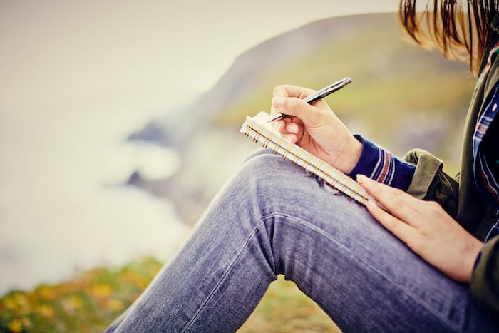 woman writing in diary sitting outside journaling ideas