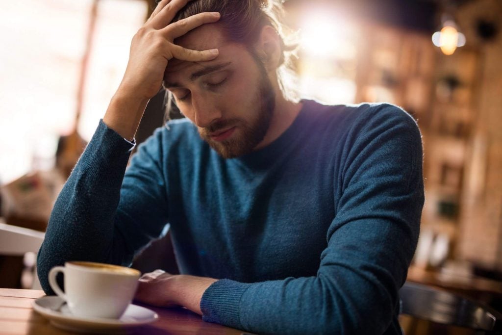 man holding head sad while drinking coffee Why Am I So Unhappy