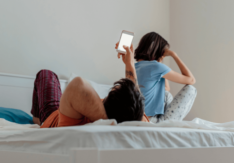 man laying on bed looking at phone women is upset Why My Husband Looks at Other Females Online