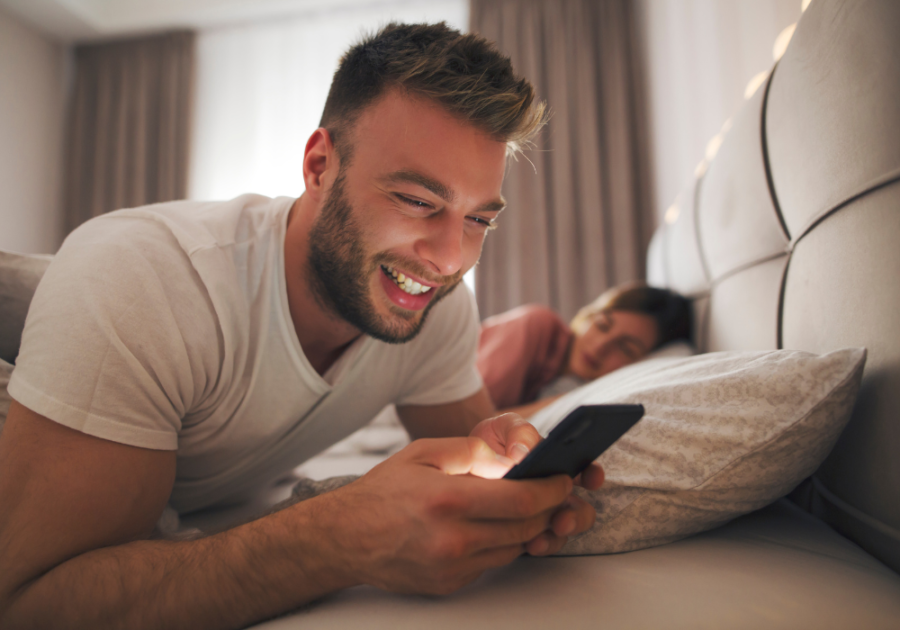 man smiling at phone while in bed signs of a player