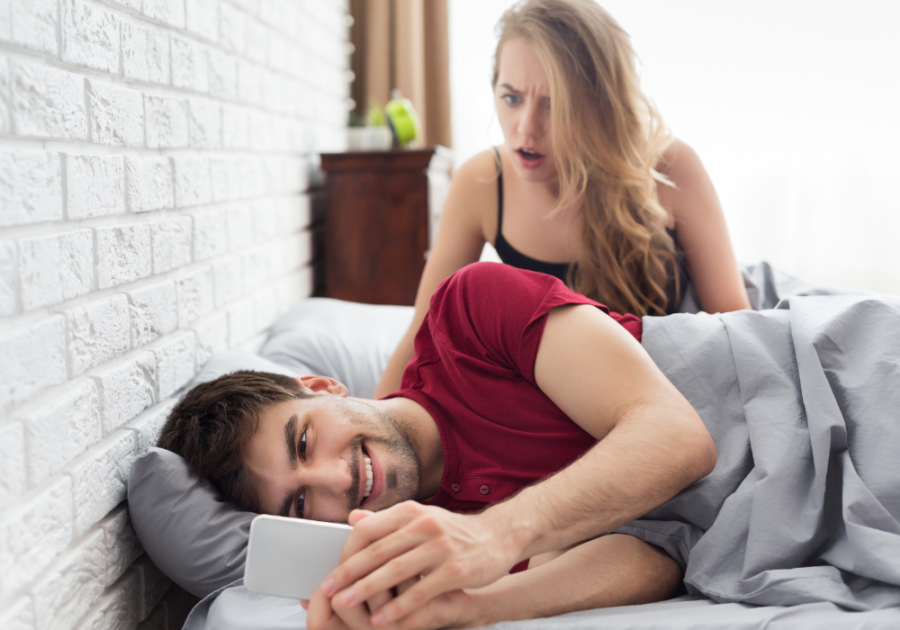 man on phone in bed with woman looking surprised Find Out If Someone Is on a Dating Site