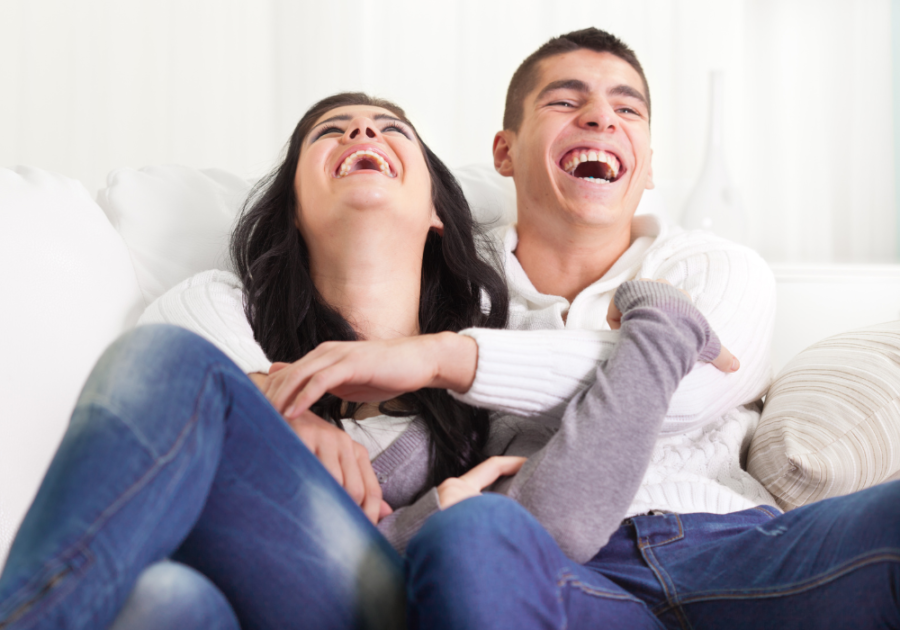 couple sitting on sofa laughing Weird Questions to Ask a Guy