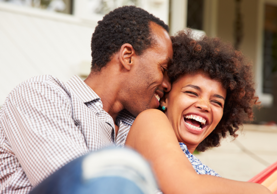 couple cuddling and laughing on sofa Juicy Questions to Ask Your Girlfriend