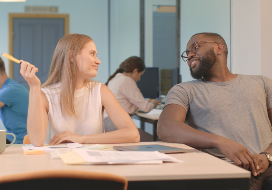 couple sitting at desks smiling at each other how to tell if a guy is interested in your or just being friendly